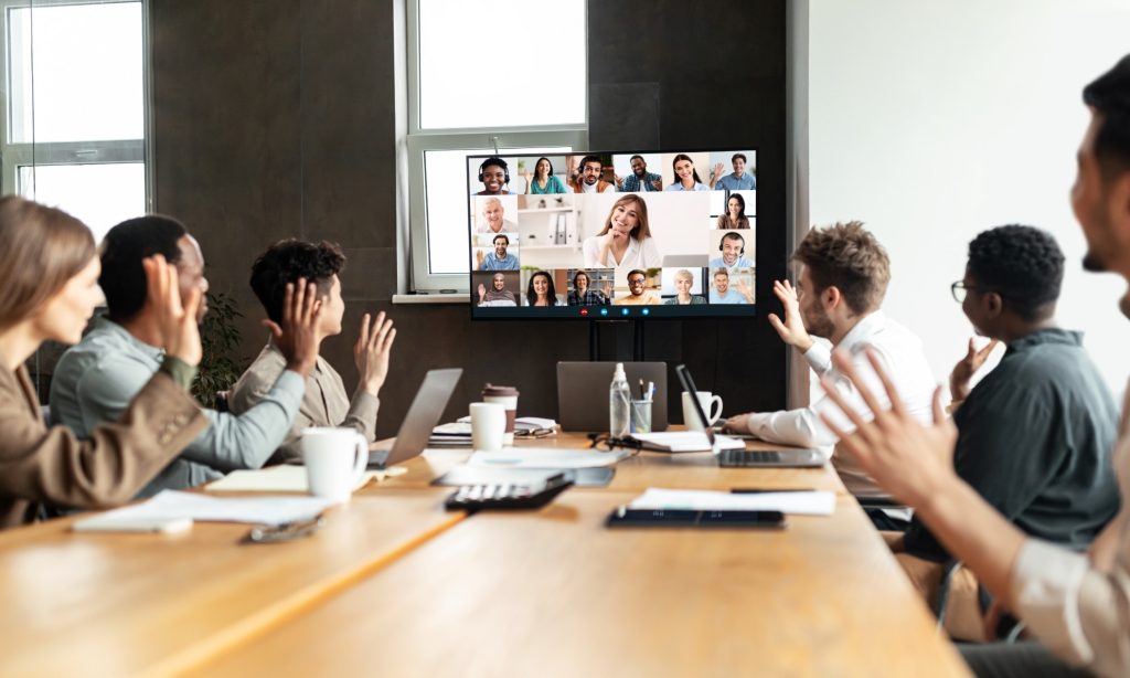 Hybrid team collaborating in a modern office while joining a video conference with remote colleagues, illustrating azure virtual desktop